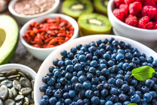 Kom met bosbessen en andere gezonde voeding voor het ontbijt met biologische supervoedingen, zoals vers fruit en zaden. Vegan Nutrition concept. — Stockfoto