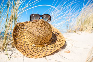 Hat and sunglasses - beach accessories on sand and blue sky. Summer holiday concept.