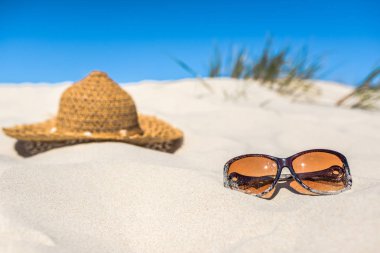 Sahilde tatil aksesuarları, güneş gözlüğü ve kumulda güneş şapkası ve mavi gökyüzü. Yaz tatili kavramı.