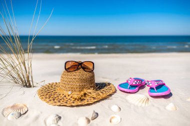 Beyaz kum ve mavi gökyüzü ile Baltık Denizi üzerinde tatil plaj aksesuarları ile arka plan. Gözlük, güneş şapkası ve parmak arası terlik..