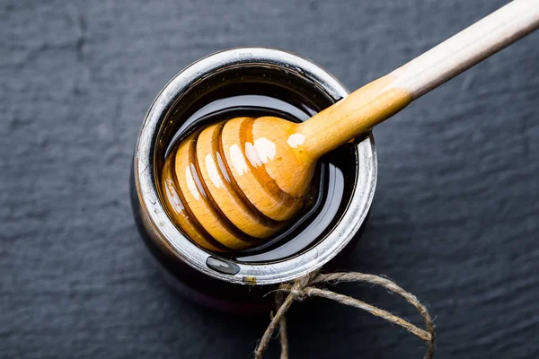 Pot en verre de miel et trempette en bois dans le miel sur fond noir — Photo