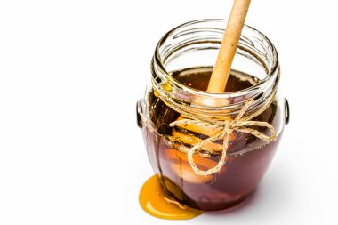 Beyaz arka planda cam bal kabına batırılmış bal ve sopa damlama