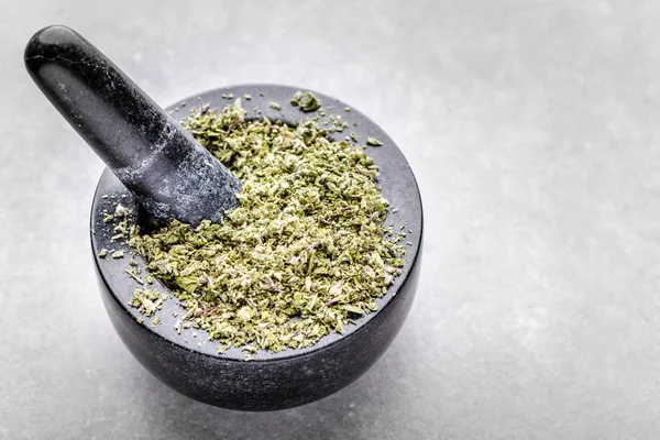 Herbal tea or dry herb in mortar, top view of aromatic spice - dried oregano, basil, marjoram or parsley - crushed leaves in mortar