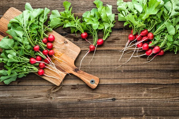 Gospodarstwo świeże organiczne rzodkiewki ogrodowe, czerwone grona na drewnianym tle — Zdjęcie stockowe