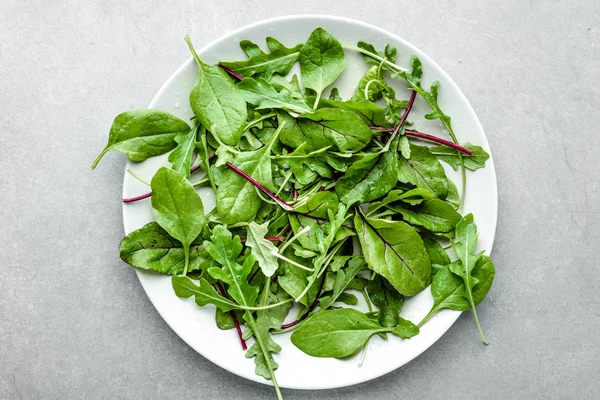 Свіжий зелений салат мікс зі шпинатом, руколою та листям буряка на тарілці, вид зверху — стокове фото