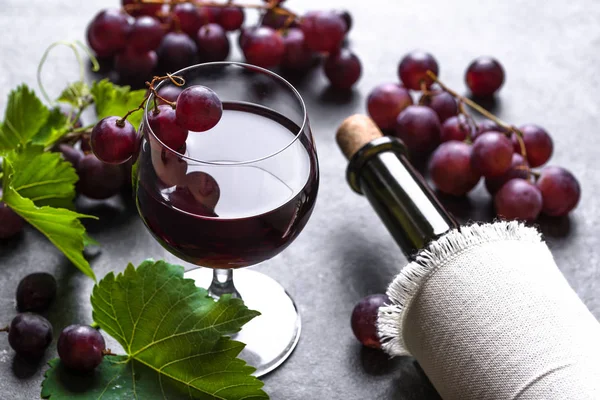 Copo de vinho com uvas vermelhas e garrafa de vinho no fundo escuro — Fotografia de Stock