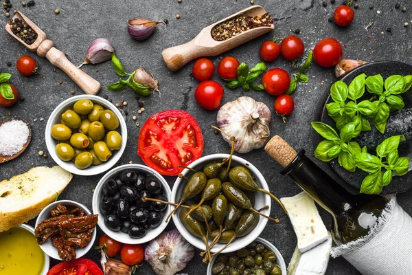 Comida mediterránea sobre fondo oscuro: hierbas, aceitunas, olil, tomate, pan, queso y botella de vino . — Foto de Stock