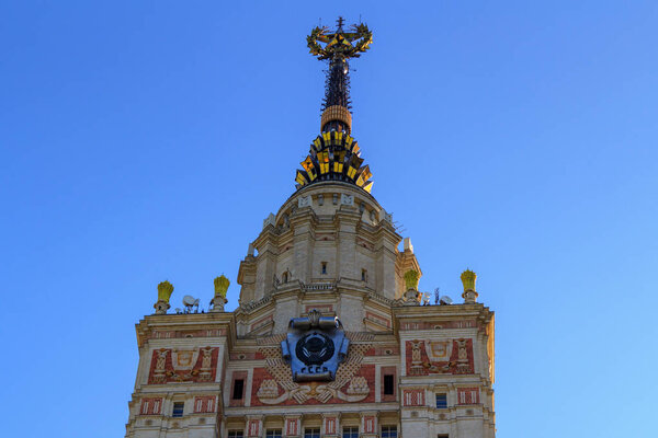 Tower of Lomonosov Moscow State University (MSU) with national emblem of USSR and star on the spire closeup on a blue sky background