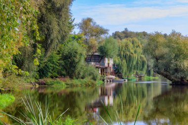 Yeşil ağaçlar karşı küçük Nehri üzerinde tekne ile eski ahşap iskele. Güneşli sonbahar sabahı, nehir manzara