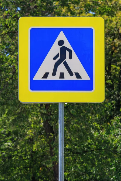 Vägskylt av crosswalk på en grå pelare mot gröna träd i solig sommar dag — Stockfoto