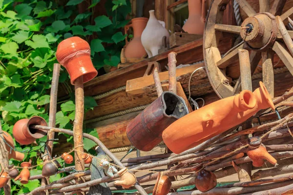 Velhos jarros de barro feitos à mão nos postes de uma cerca trançada contra a parede de uma casa de aldeia em dia ensolarado — Fotografia de Stock