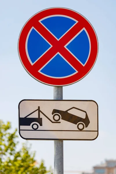 Road sign prohibiting the stopping of the car with a tow truck signboard against blue sky in sunny day closeup — Stock Photo, Image