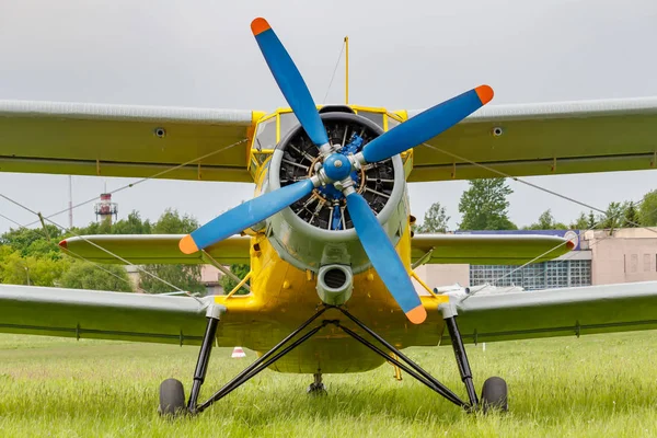 Soviet aircraft biplane Antonov AN-2 with blue four blade propeller and yellow fuselage parked on a green grass of airfield closeup — Stock Photo, Image