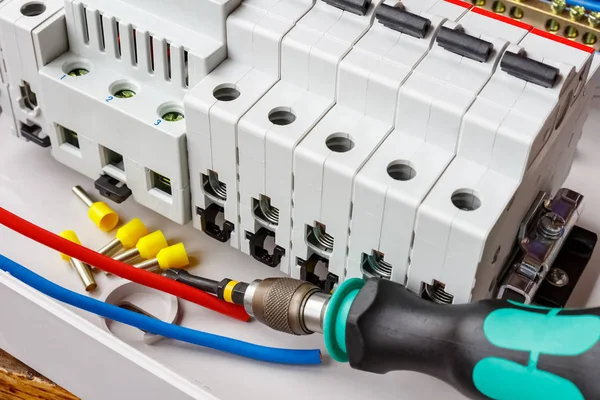 Automatic circuit breakers installed on DIN rail in white plastic mounting box on a background of wires and screwdriver