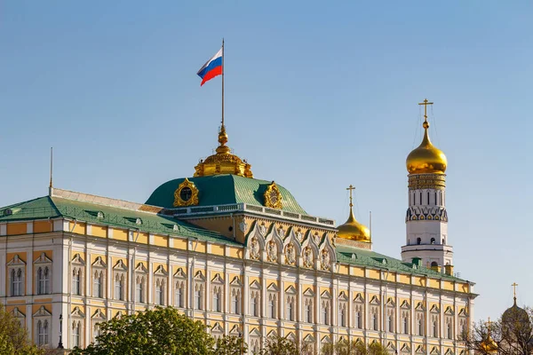 Moscú, Rusia - 01 de mayo de 2019: Vista del Palacio del Gran Kremlin con la bandera ondeante de la Federación Rusa e Iván el Gran Campanario del Kremlin de Moscú sobre un fondo azul del cielo Imagen De Stock