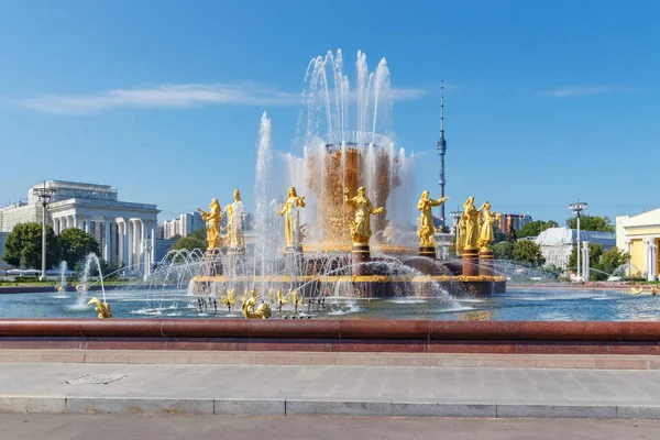 Moscú, Rusia - 22 de julio de 2019: Fuente de la Amistad de los Pueblos en un fondo de la torre de televisión Ostankinskaya y pabellones en el parque VDNH en Moscú en el soleado día de verano contra el cielo azul — Foto de Stock