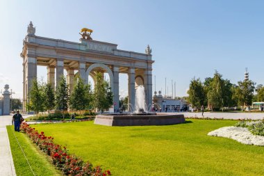 Moskova, Rusya - 22 Temmuz 2019: Güneşli yaz sabahında ana giriş arkına karşı Moskova'daki Vdnh parkında yeşil çimler üzerinde çeşme çalışması
