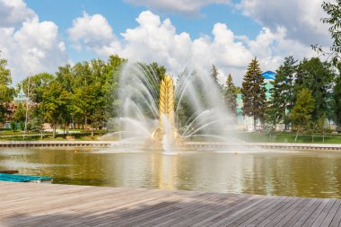 Moskova, Rusya - 22 Temmuz 2019: Güneşli yaz gününde mavi gökyüzüne karşı Moskova'daki Vdnh parkında Kamensky göletinde Altın Başak çeşmesi. Tekne istasyonunun iskelesinden görünüm