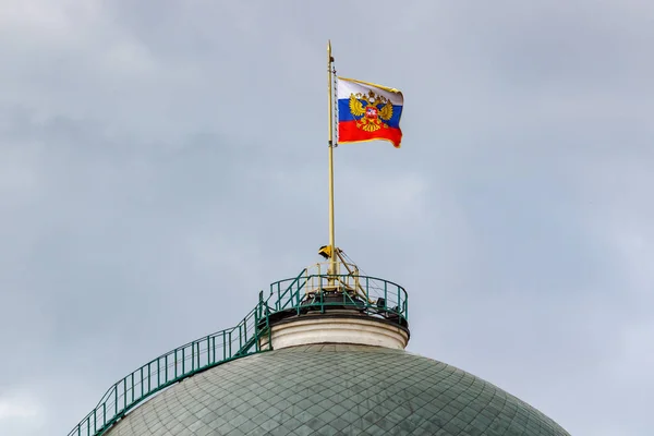 Flag of Russian Federation with gilded coat of arms waving on the dome of Senate Palace of Moscow Kremlin