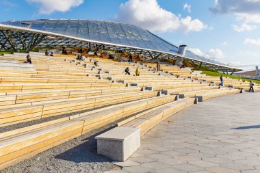 Moskova, Rusya - 08 Ekim 2019: Güneşli sonbahar gününde Zaryadye Parkı 'nın büyük amfitiyatrosundaki ahşap banklarda dinlenen insanlar. Zaryadye Parkı Moskova 'da popüler bir turistik beldedir.
