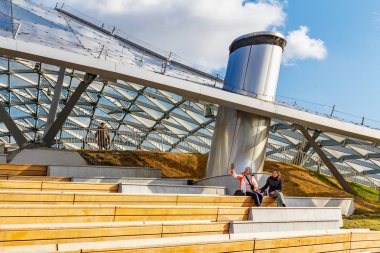 Moskova, Rusya - 08 Ekim 2019: İki kadın güneşli sonbahar gününde Zaryadye Park 'taki büyük amfitiyatroya karşı ahşap bankta selfie çekti. Zaryadye Parkı Moskova 'da popüler bir turistik yerdir.