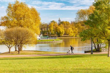 Moskova, Rusya - 16 Ekim 2019: Güneşli bir sonbahar gününde göl kıyısında yürüyen bebek arabalı bir adam. Tsaritsyno Parkı Moskova 'da yürümek için popüler bir yerdir.