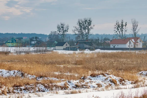 Snow covered field and village houses in winter day. Country landscape in winter