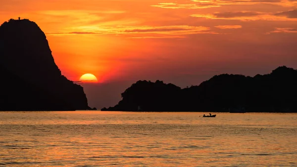 Half of beautiful sun and white cloud in the orange sky with silhouette fisherman on the long tail boat and islands in the sea as foreground. Warm tone. Rule of third composition.