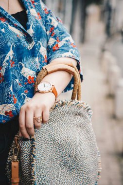 sokak tarzı moda ayrıntılar. yakın çekim, moda blogger bir yaz gömlek ve bir güzel yuvarlak hasır çanta tutan bir beyaz ve kahverengi analog kol saati takıyor. mükemmel yaz moda aksesuarları.