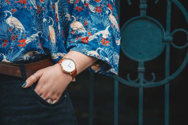 sokak tarzı moda ayrıntılar. yakın çekim, moda blogger bir yaz gömlek ve bir güzel yuvarlak hasır çanta tutan bir beyaz ve kahverengi analog kol saati takıyor. mükemmel yaz moda aksesuarları.