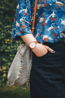 sokak tarzı moda ayrıntılar. yakın çekim, moda blogger bir yaz gömlek ve bir güzel yuvarlak hasır çanta tutan bir beyaz ve kahverengi analog kol saati takıyor. mükemmel yaz moda aksesuarları.