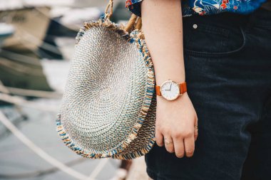 sokak tarzı moda ayrıntılar. yakın çekim, moda blogger bir yaz gömlek ve bir güzel yuvarlak hasır çanta tutan bir beyaz ve kahverengi analog kol saati takıyor. mükemmel yaz moda aksesuarları.
