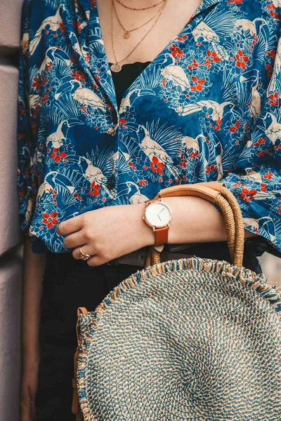 street style fashion details. close up, fashion blogger wearing a summer shirt and a white and brown analog wrist watch, holding a beautiful round straw purse. perfect summer fashion accessories.