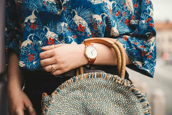 street style fashion details. close up, fashion blogger wearing a summer shirt and a white and brown analog wrist watch, holding a beautiful round straw purse. perfect summer fashion accessories.