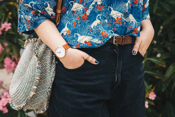 street style fashion details. close up, fashion blogger wearing a summer shirt and a white and brown analog wrist watch, holding a beautiful round straw purse. perfect summer fashion accessories.