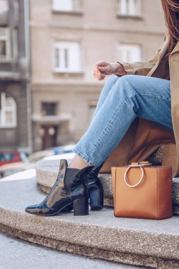 sokak tarzı bej bir palto, denim jeans, ayak bileği botları, kedi göz güneş gözlüğü ve Metal kolu Deri tote çanta çekici bir kadın portresi. moda kıyafet güneşli bir bahar için mükemmel