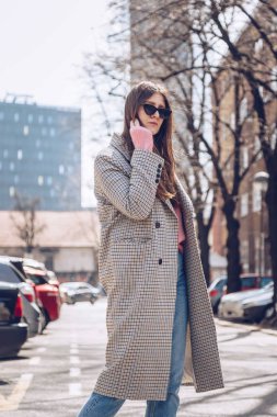 yumuşak pembe kazak ve pepita houndstooth desen açık palto giyen moda kadın. kedi göz güneş gözlüğü ile accessorized. moda sokak stili.