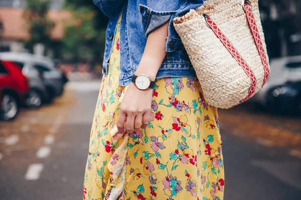 street style fashion details. woman wearing a summer dress and a white and black analog wrist watch, holding a trendy beach straw purse. perfect summer 2018 fashion accessories.