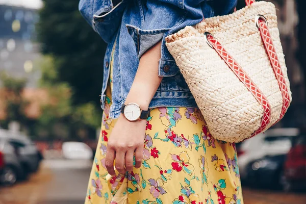 street style fashion details. woman wearing a summer dress and a white and black analog wrist watch, holding a trendy beach straw purse. perfect summer 2018 fashion accessories.