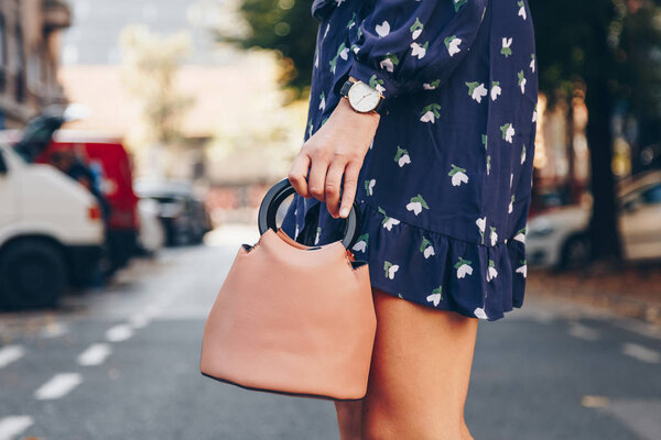 street style fashion details. close up, young fashion blogger wearing a floral dress, and a black and white analog wrist watch. checking the time, holding a beautiful pink purse.