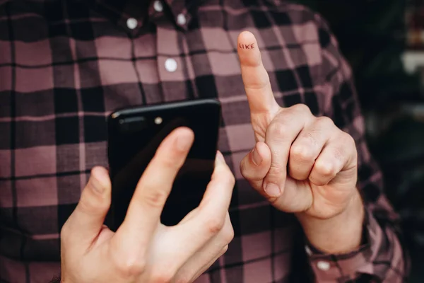 close up of man using smartphone. concept of phone addiction. young man typing and browsing social media on his phone. word like written on finger.