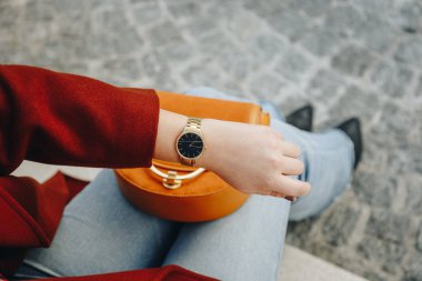 street style fashion details. close up, young fashion blogger wearing brown winter coat, and a black and golden analog wrist watch. checking the time, holding a beautiful suede leather purse. clipart