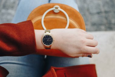 sokak tarzı moda ayrıntılar. genç moda blogger giyen kahverengi kış ceket ve siyah ve altın analog Bilek izlemek kapatın. bir güzel süet deri çanta elinde süre kontrol.