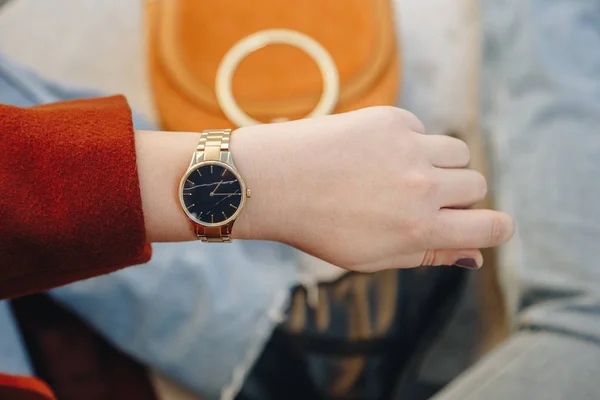 street style fashion details. close up, young fashion blogger wearing brown winter coat, and a black and golden analog wrist watch. checking the time, holding a beautiful suede leather purse.