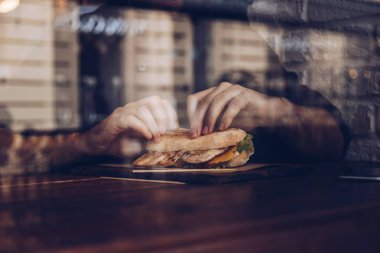 pencerenin yanında oturan bir modern fast food restoran sağlıklı tavuk sandviç yiyerek bir adamın kapatın. pencereden şehir yansımaları ile vurdu