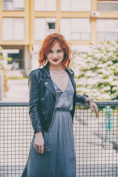 street style fashion potrait of a beautiful young red haired woman wearing a leather jacket in the city