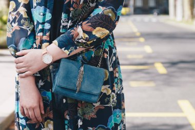sokak tarzı moda ayrıntılar. yakın, çiçek bir ceket ve beyaz ve altın analog kol saati giyen genç moda blogger. bir güzel süet deri çanta elinde süre kontrol.