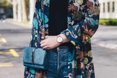 sokak tarzı moda ayrıntılar. yakın, çiçek bir ceket ve beyaz ve altın analog kol saati giyen genç moda blogger. bir güzel süet deri çanta elinde süre kontrol.
