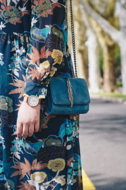 sokak tarzı moda ayrıntılar. yakın, çiçek bir ceket ve beyaz ve altın analog kol saati giyen genç moda blogger. bir güzel süet deri çanta elinde süre kontrol.