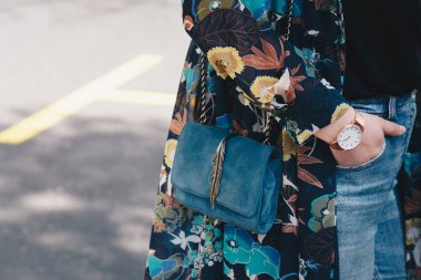 sokak tarzı moda ayrıntılar. yakın, çiçek bir ceket ve beyaz ve altın analog kol saati giyen genç moda blogger. bir güzel süet deri çanta elinde süre kontrol.